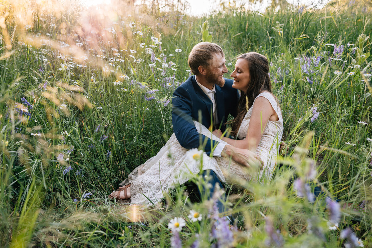 Bride sits on grooms lap in the middle of wildflowers in north Idaho.