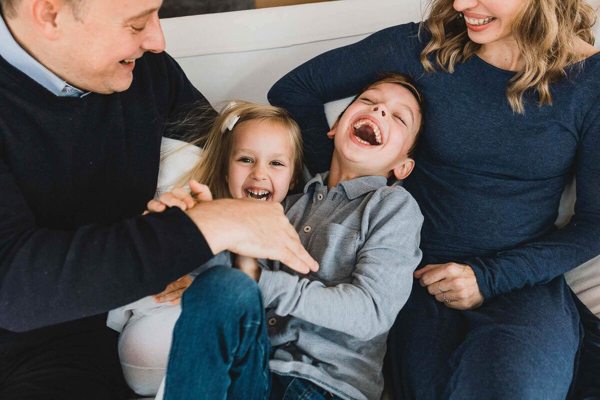 Mom and dad tickling siblings on white couch. Laughter and connection captured by Cleveland family photographer.
