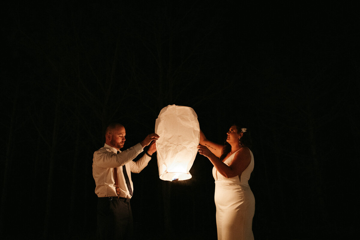 Bride and groom in wedding attire holding a paper lantern during their send off at the reception