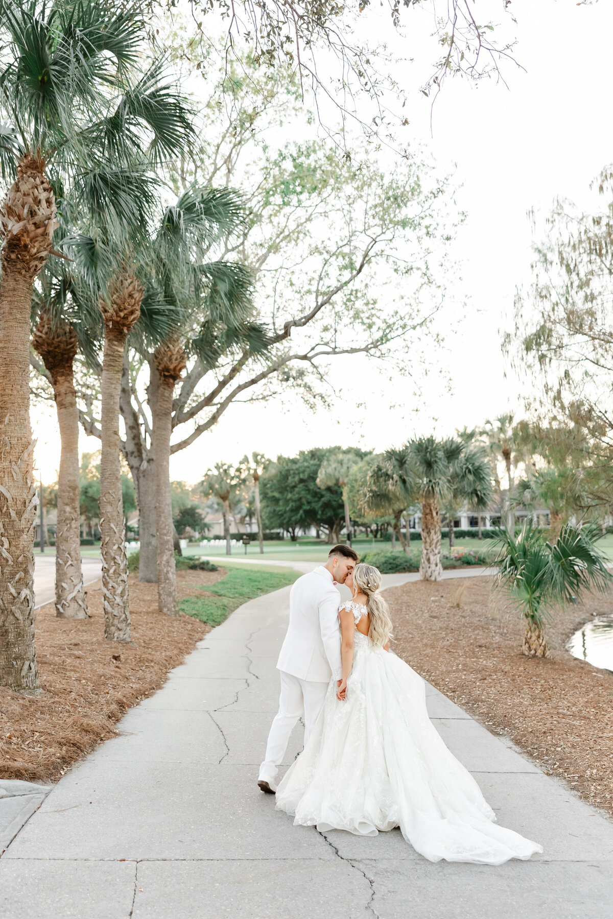 bride and groom kissing on a path next to palm trees taken by wedding photographer in florida