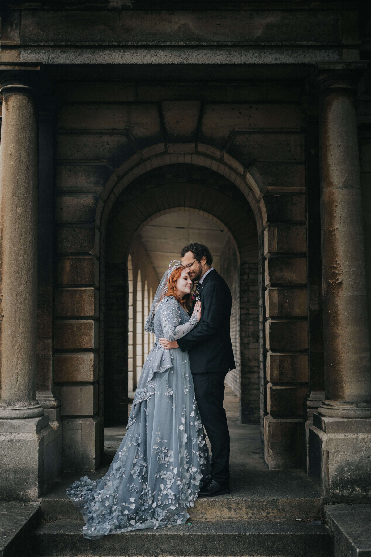 A bride in a grey dress with her groom in an archway