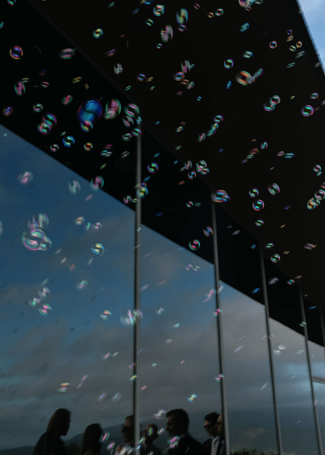 Bubbles reflecting light against a glass wall with silhouettes of guests