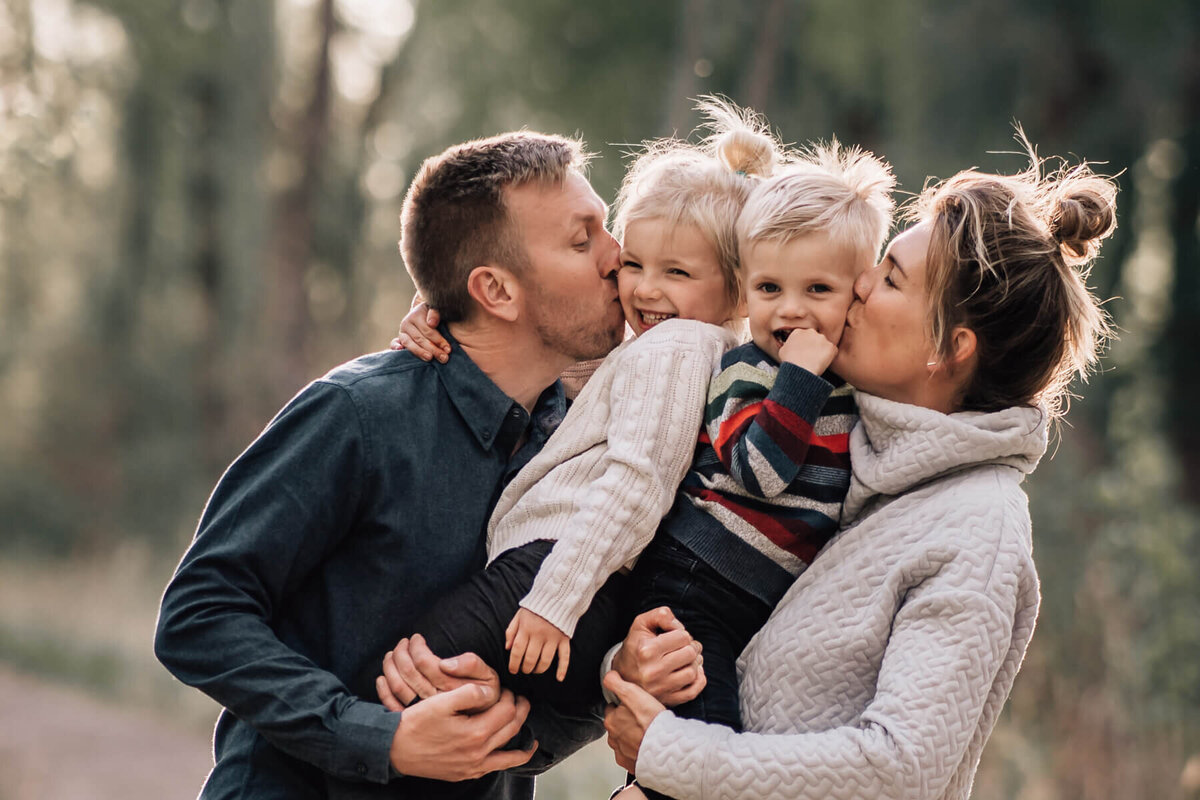 Two parents hold their young kids and kiss them both on the cheek at Roberts Bird Sanctuary in Minneapolis, Minnesota.