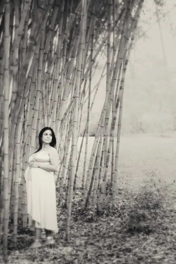 A pregnant woman standing next to bamboo trees.