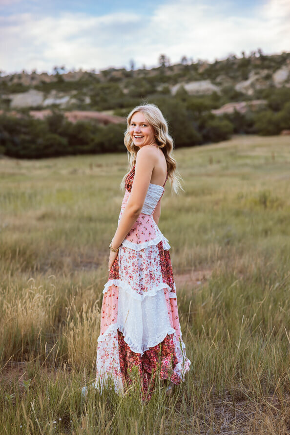Girl in pink patchwork dress dances in grassy field.