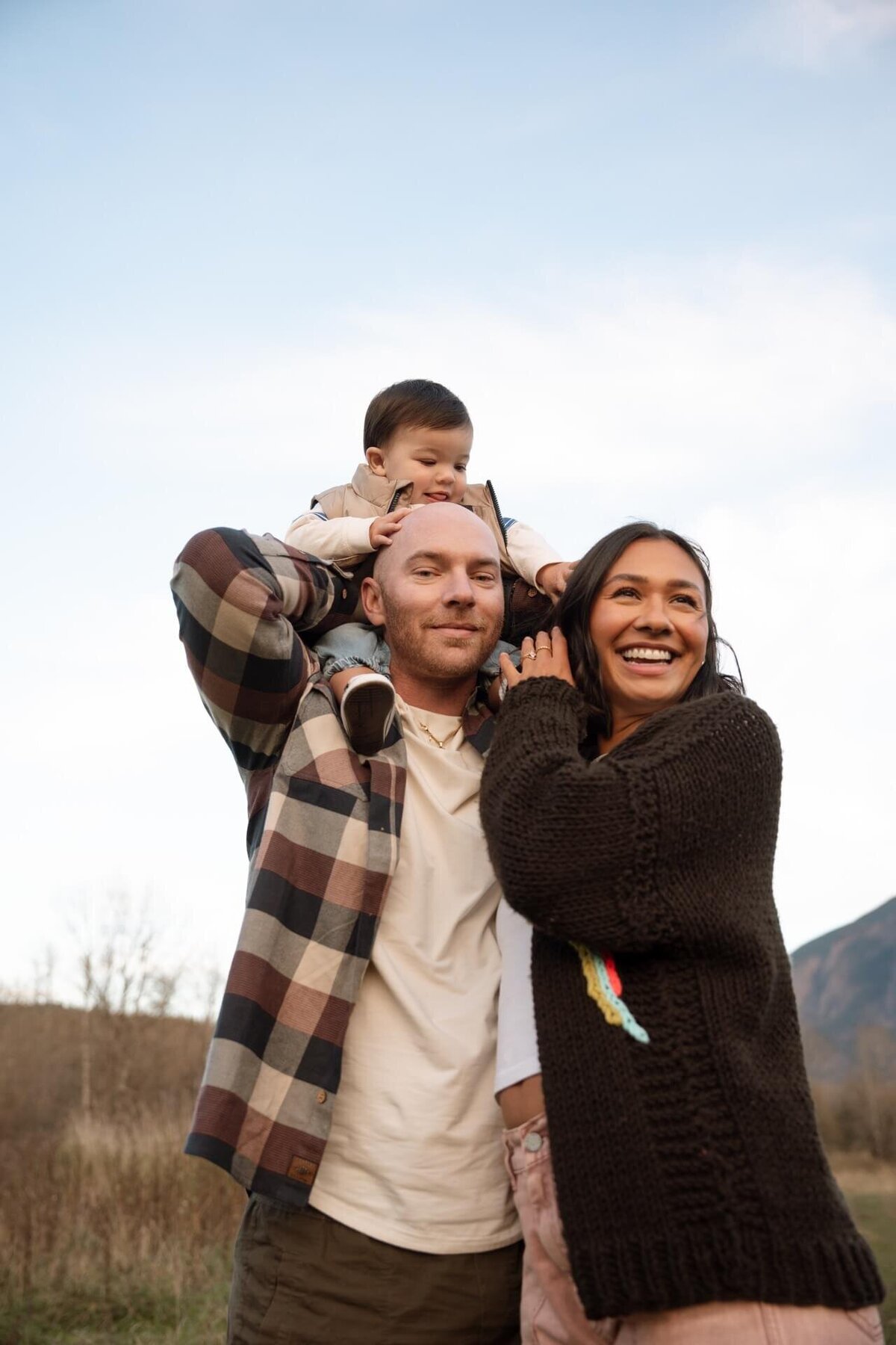 a male and female with a son on their shoulders near a mountain