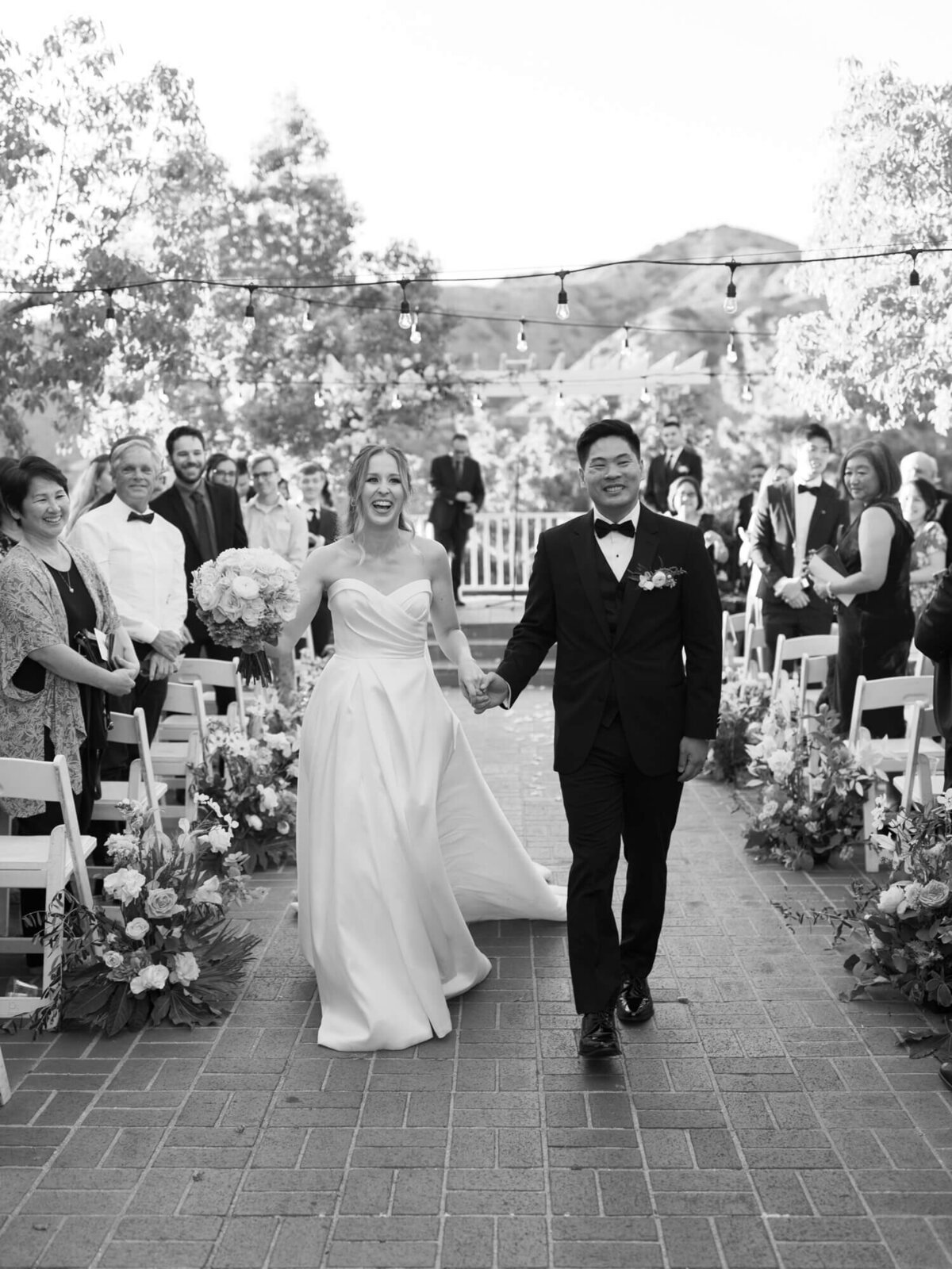 black and white photo of bride and groom exiting the ceremony and cheering