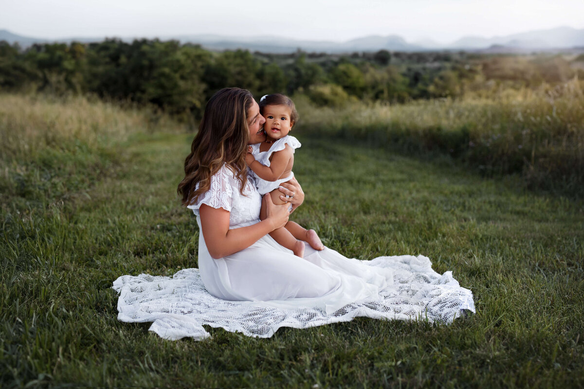 mother wearing a white dress with her toddler in the middle of a wheat field at sunset at  a mommy and me session