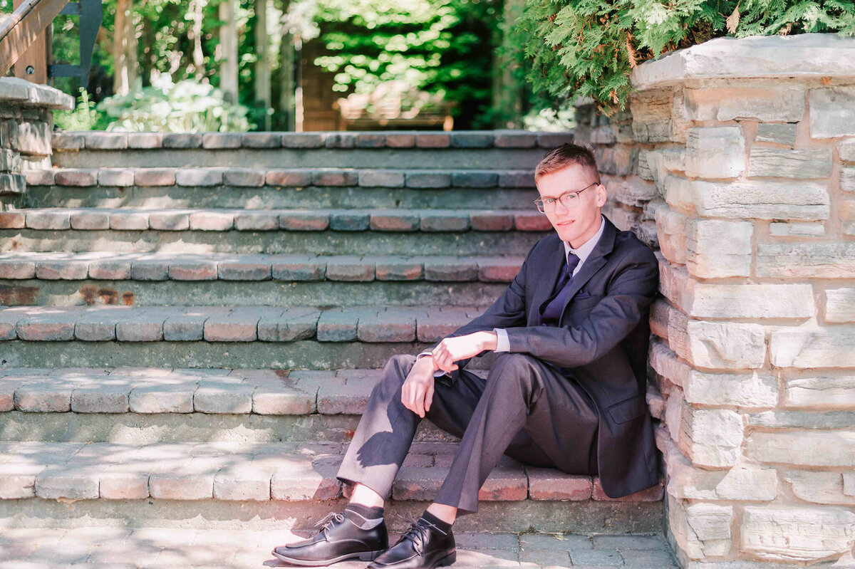 A young man sitting on some stairs and leaning on a stone wall.