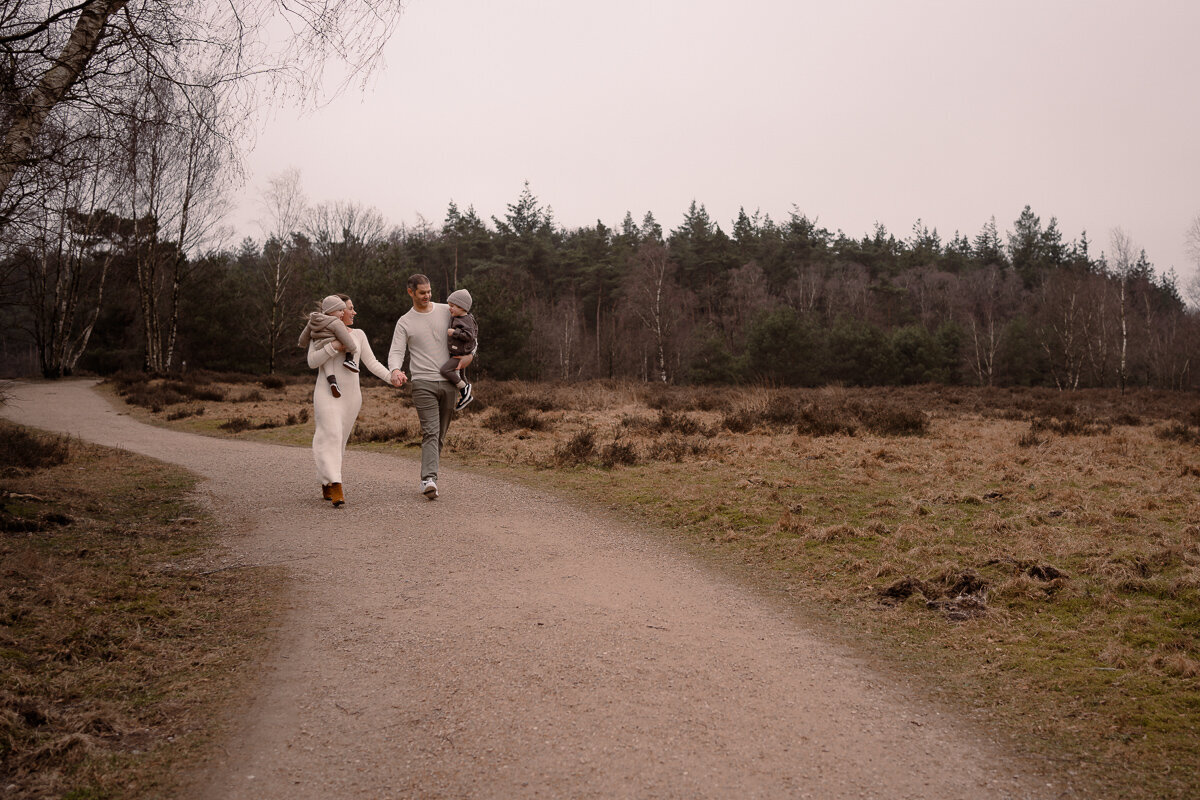 Moeder en vader lopen met hun twee kinderen op de arm hand in hand tijdens een gezinshoot