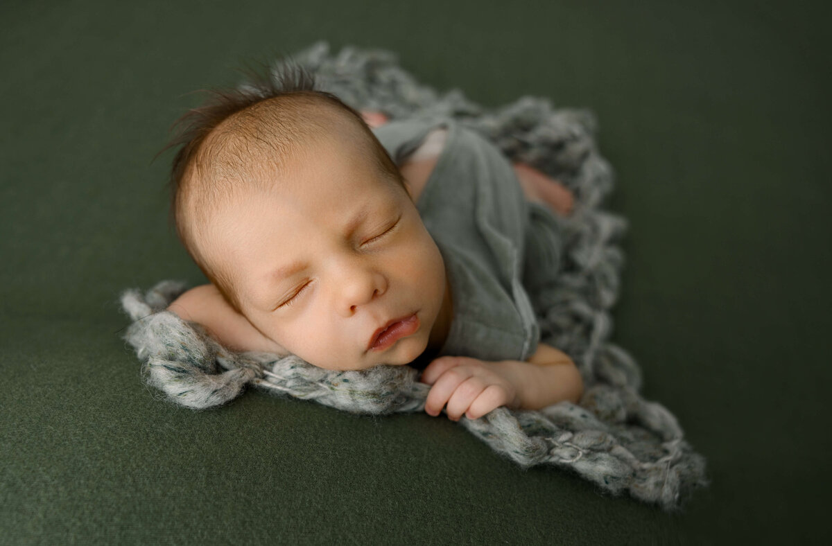 A newborn baby boy laying on a green knit blanket