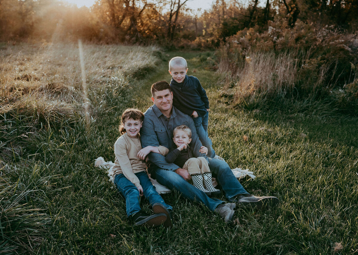 Three boys climb all over their dad, as if he's a jungle gym, wearing beautiful denim and navy blue colors during their fall photography session on their own slice of Heaven in Denver, Colorado.