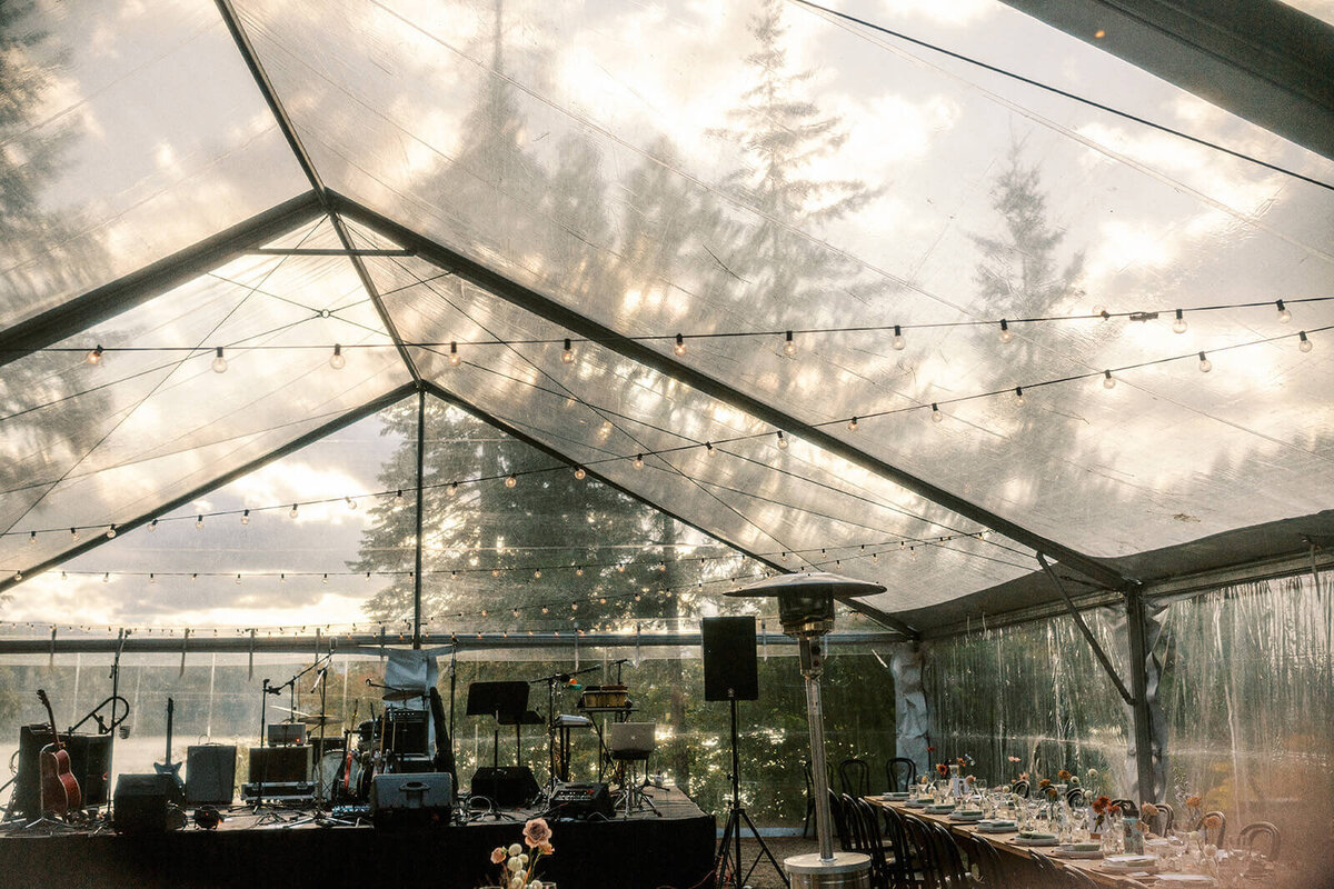 Inside a clear wedding tent showing the set up for a band and lights strung up.