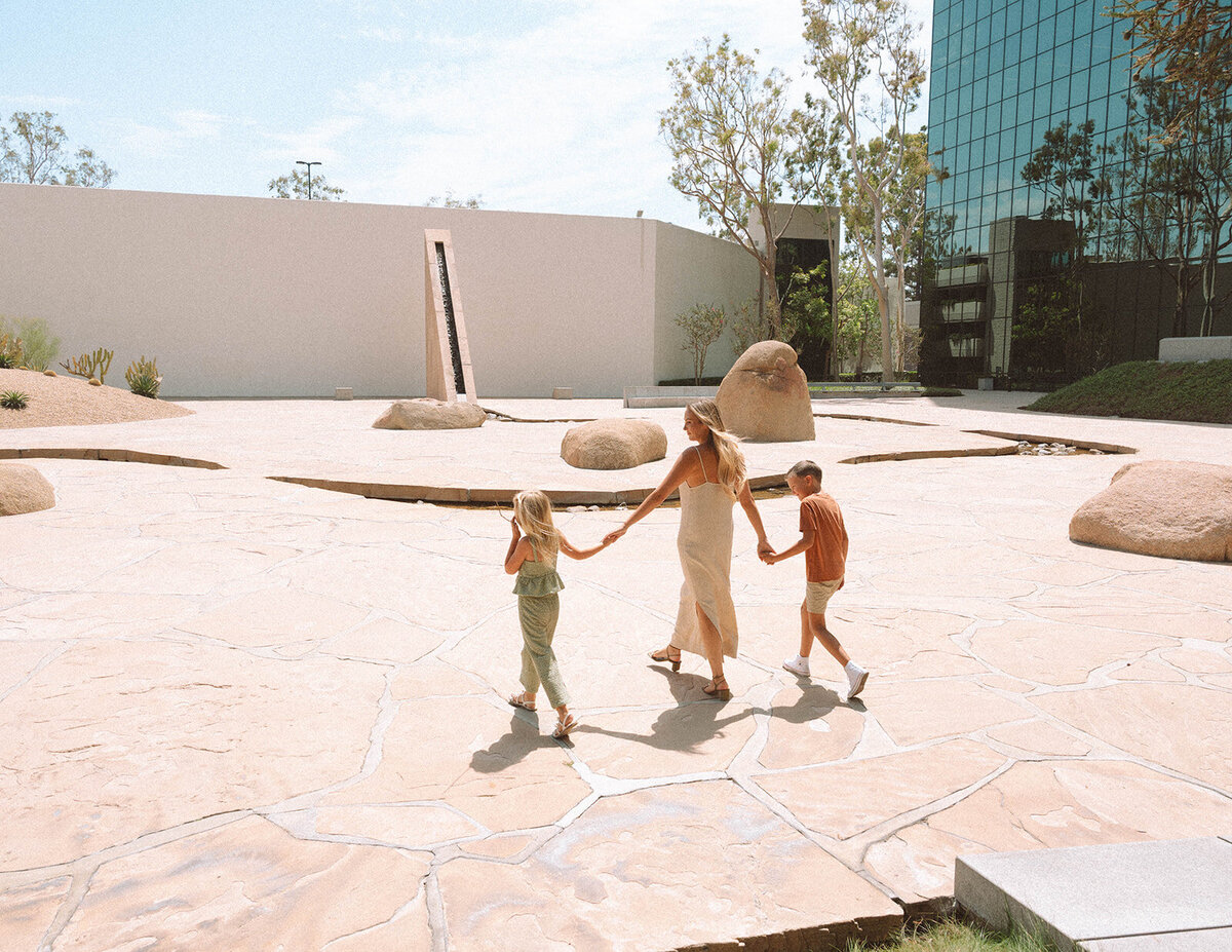Irvine family photography at Noguchi Garden with a mom walking hand in hand with her two kids across the stone plaza.