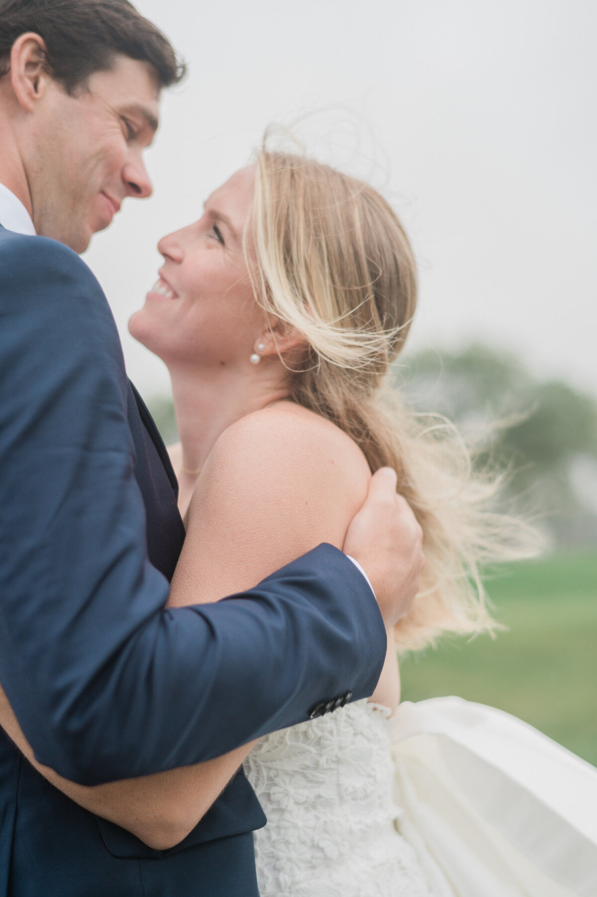 The newlyweds hold each other closely, smiling as the wind blows through the bride's hair 