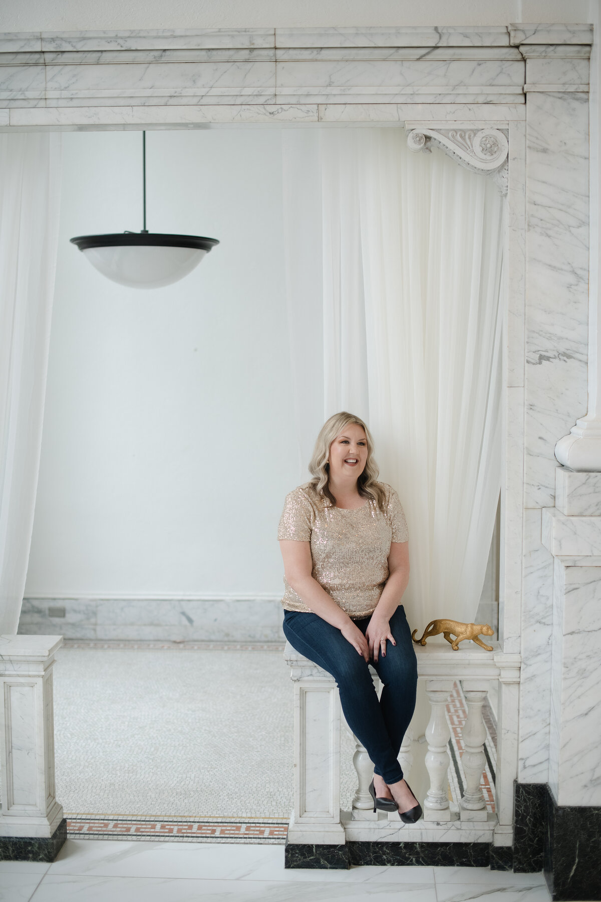 Career coach, Melissa Lawrence, sits on marble wall in sparkly blouse
