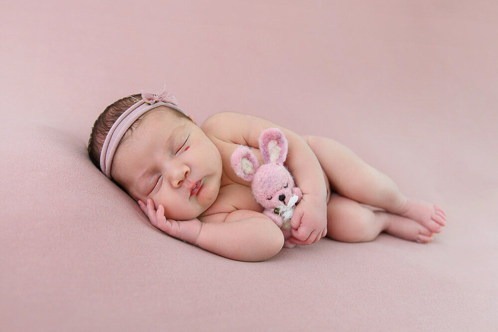 baby girl laying on her side holding a tiny pink bunny.