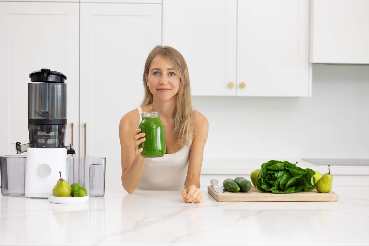 Olivia Budgen smiling and leaning on a kitchen bench holding a healthy green juice