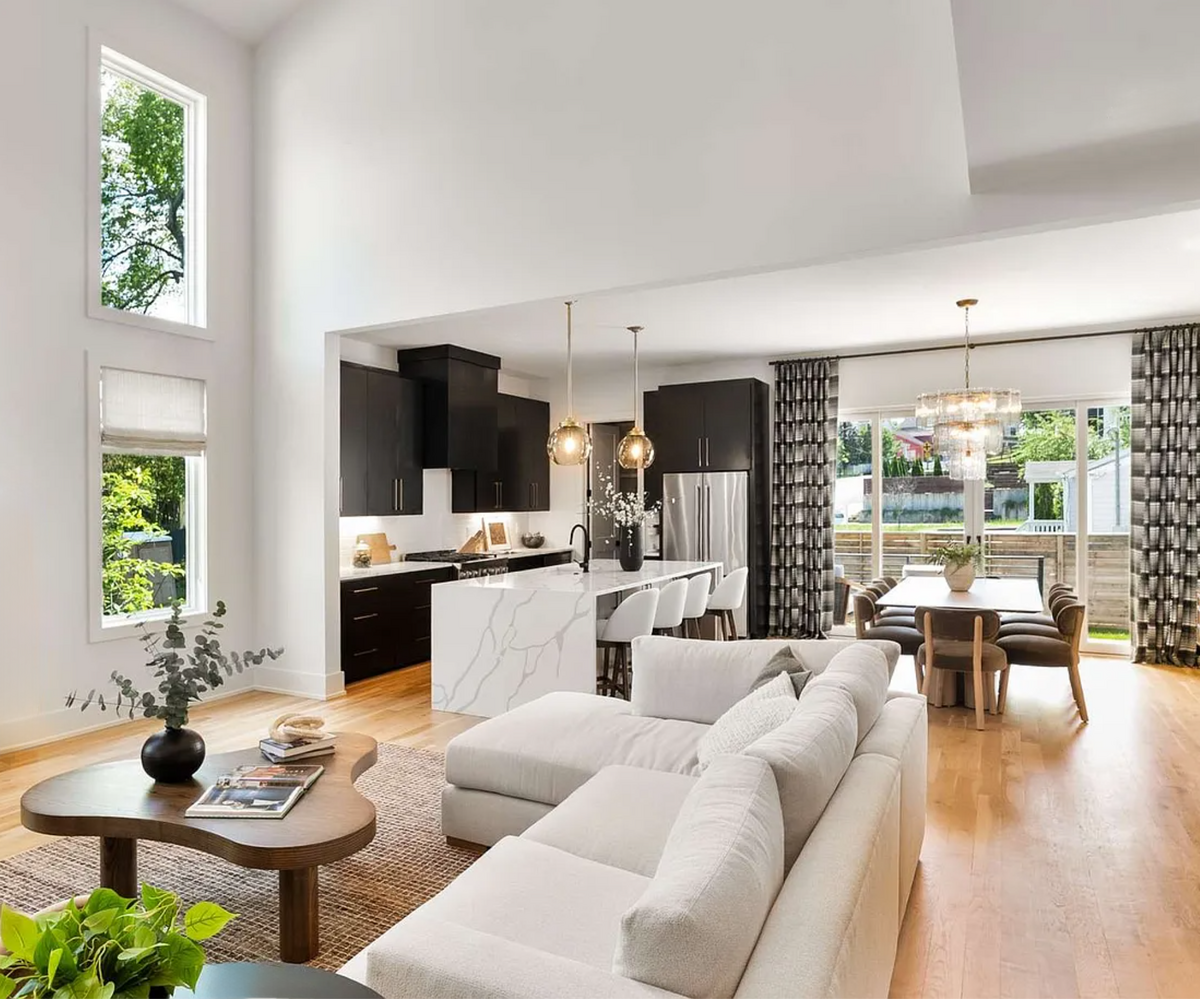 Sunlit open-concept space with quartz waterfall island, black kitchen cabinets, white sectional, and modern dining area with statement chandelier