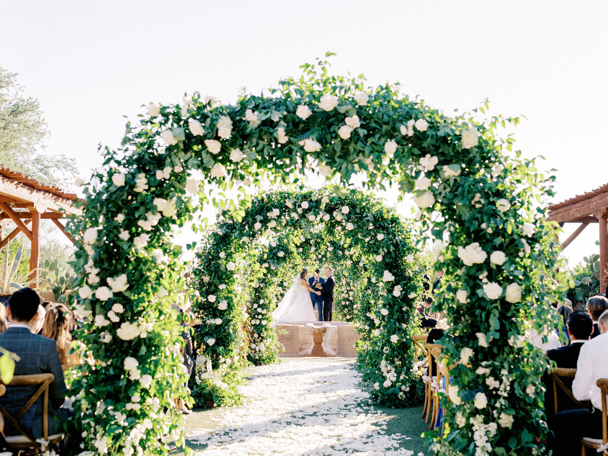 A romantic wedding ceremony under a beautifully designed floral arch, as the bride and groom exchange heartfelt vows.