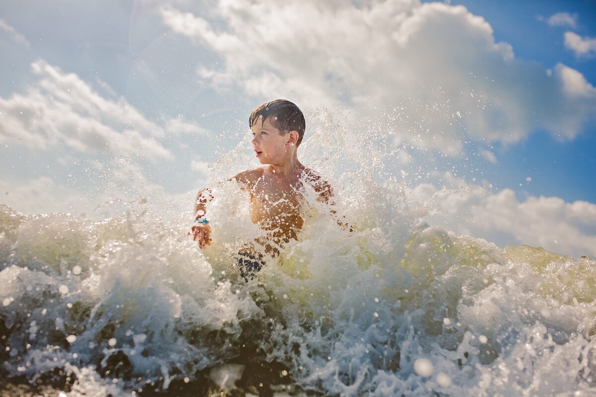 A vacation photographer captures a young boy playing in the water at the beach.
