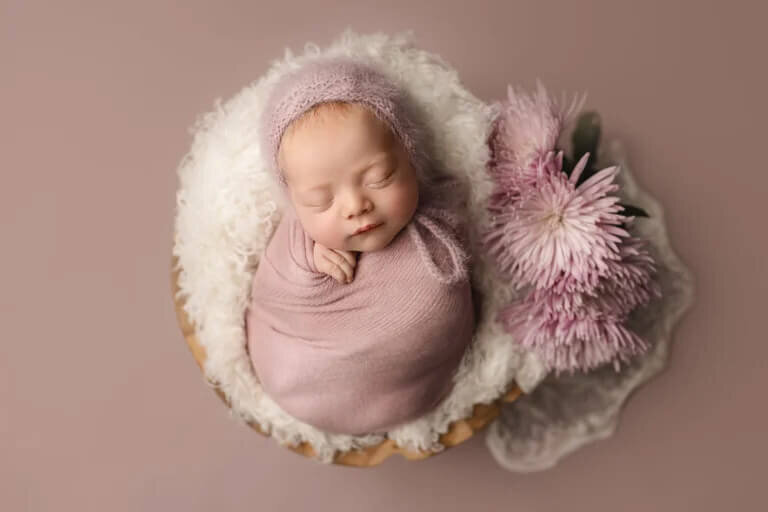 Newborn girl on pink background sleeping in a bowl with flowers