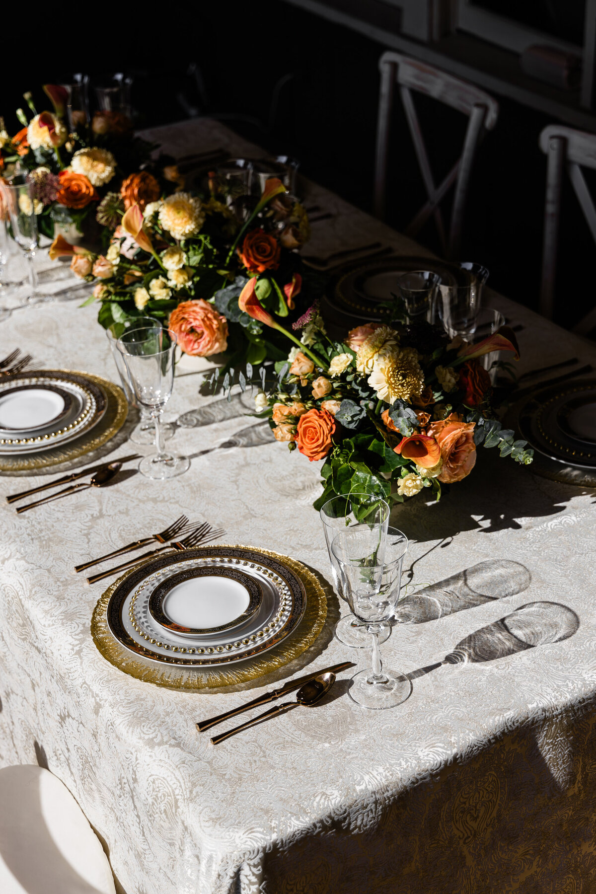 moody overcast view of four plate mixed metals place setting with four piece rose gold flatware set and a orange rose and calla lily centerpiece