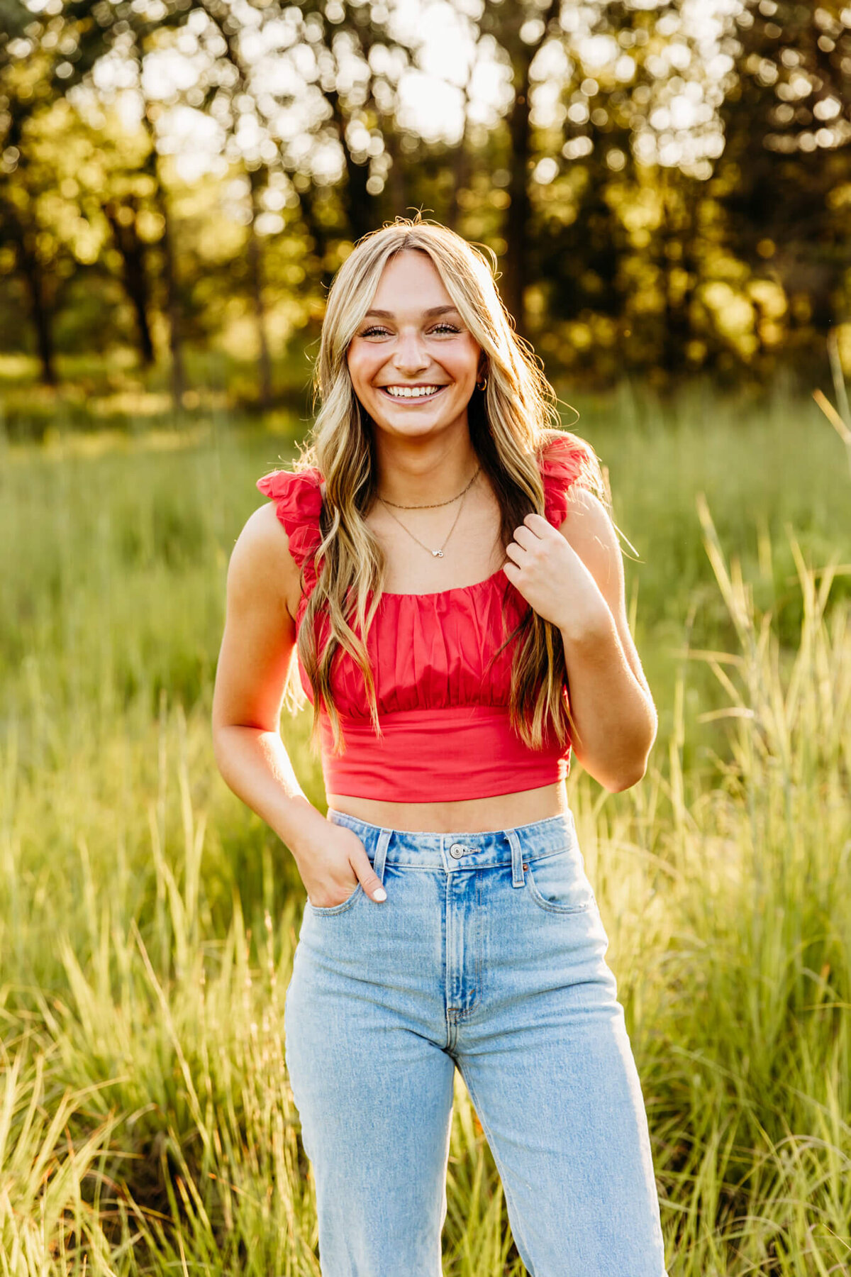 cute girl teenager in red crop top and light jeans running fingers through her hair and smiling by Ashley Kalbus