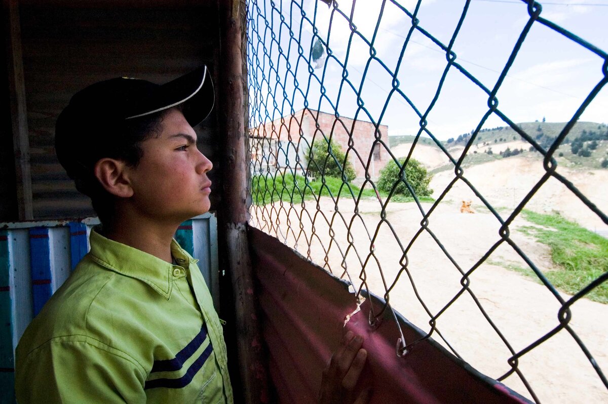 Boy from rural mountain village in Columbia stares through wire fence in interesting editorial portrait