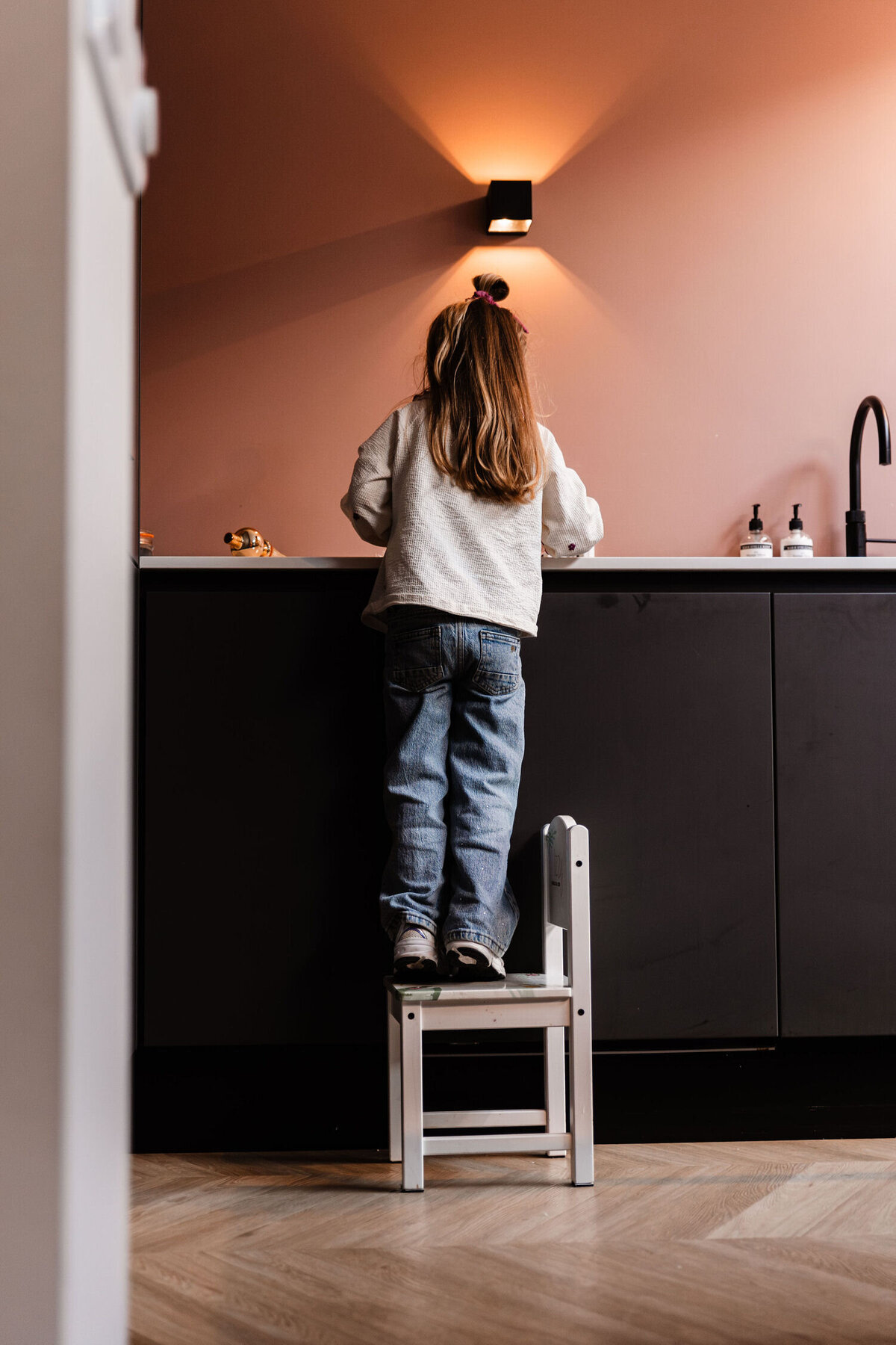 meisje staat op klein stoeltje aan het aanrecht