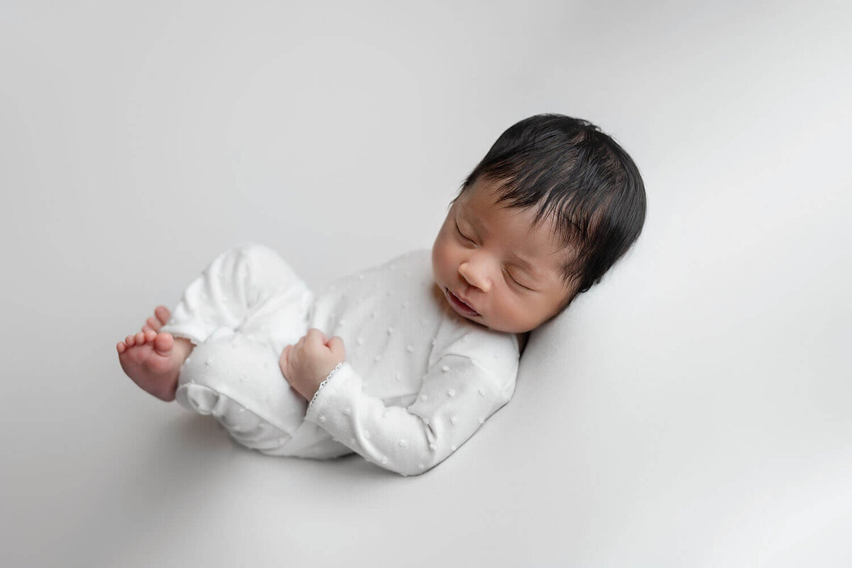 A newborn baby sleeps on its back in a studio in a white onesieNew Orleans Newborn Photographer