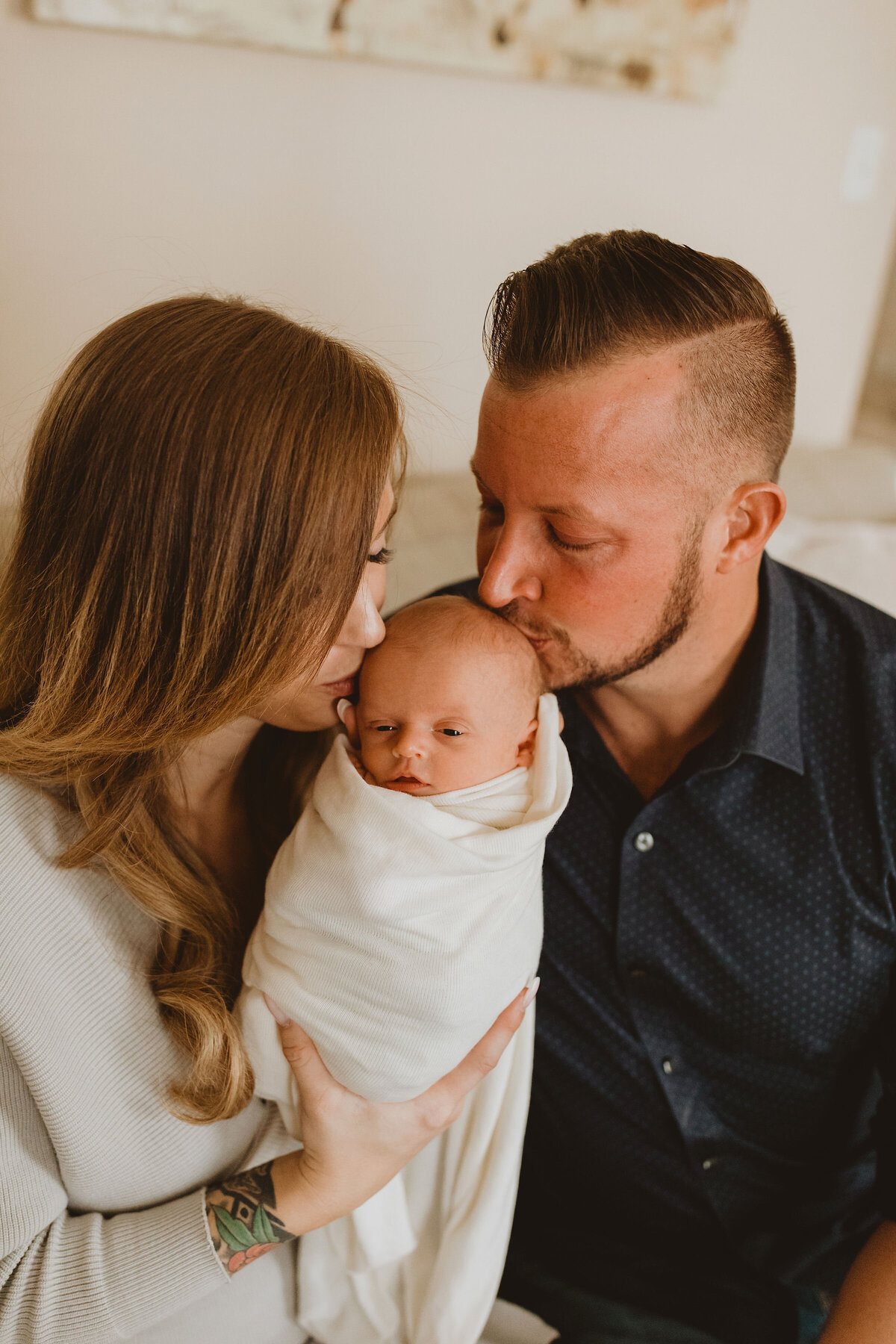 mom and dad kiss baby's head