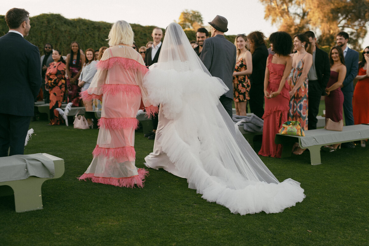 Stylish bride in a dramatic tulle gown walks down the aisle surrounded by guests, illustrating bold fashion moments in Seattle wedding photography.
