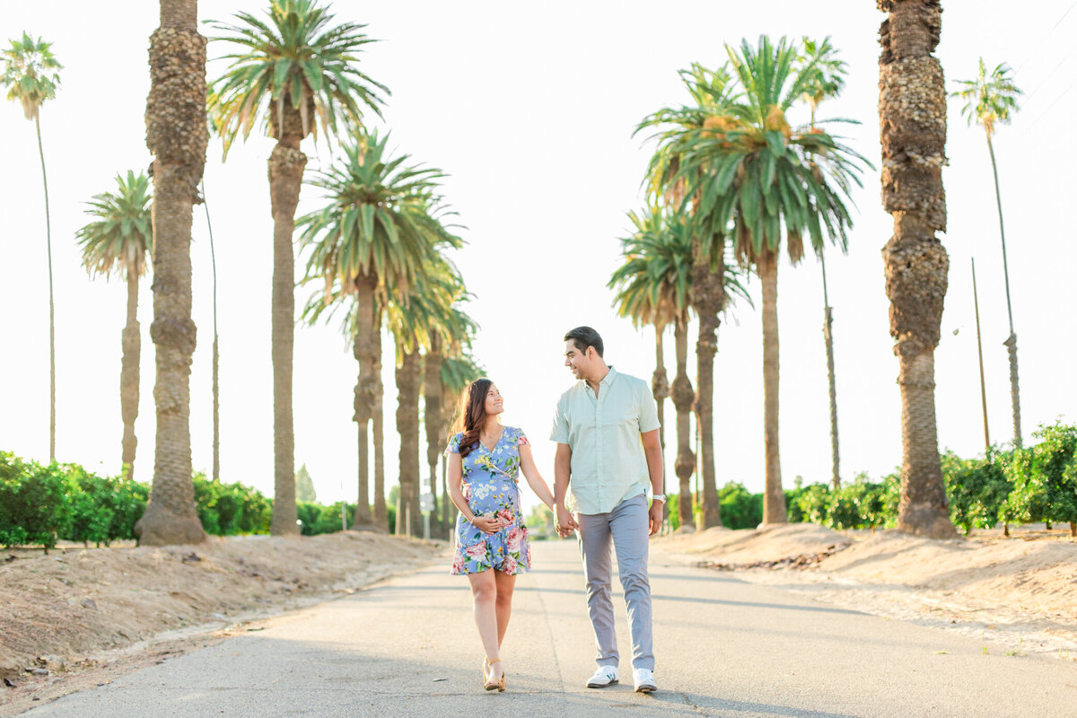 couple holds belly and walks through palm trees