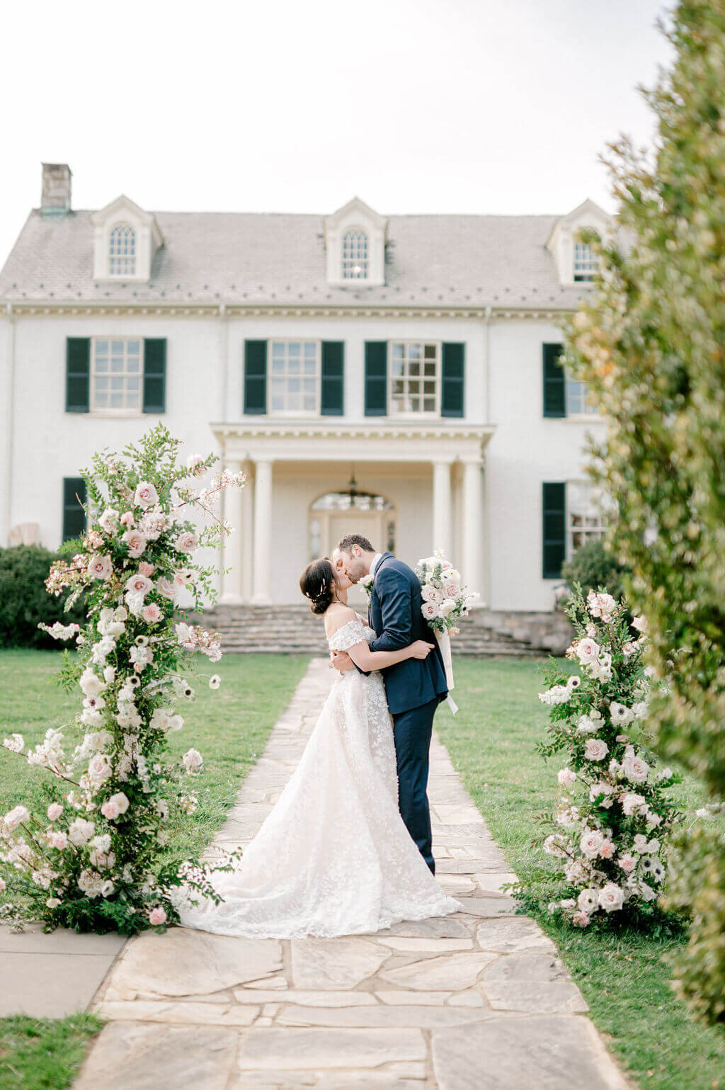 Kissing  wedding photo of bride and groom at Rust Manor house with flower arch