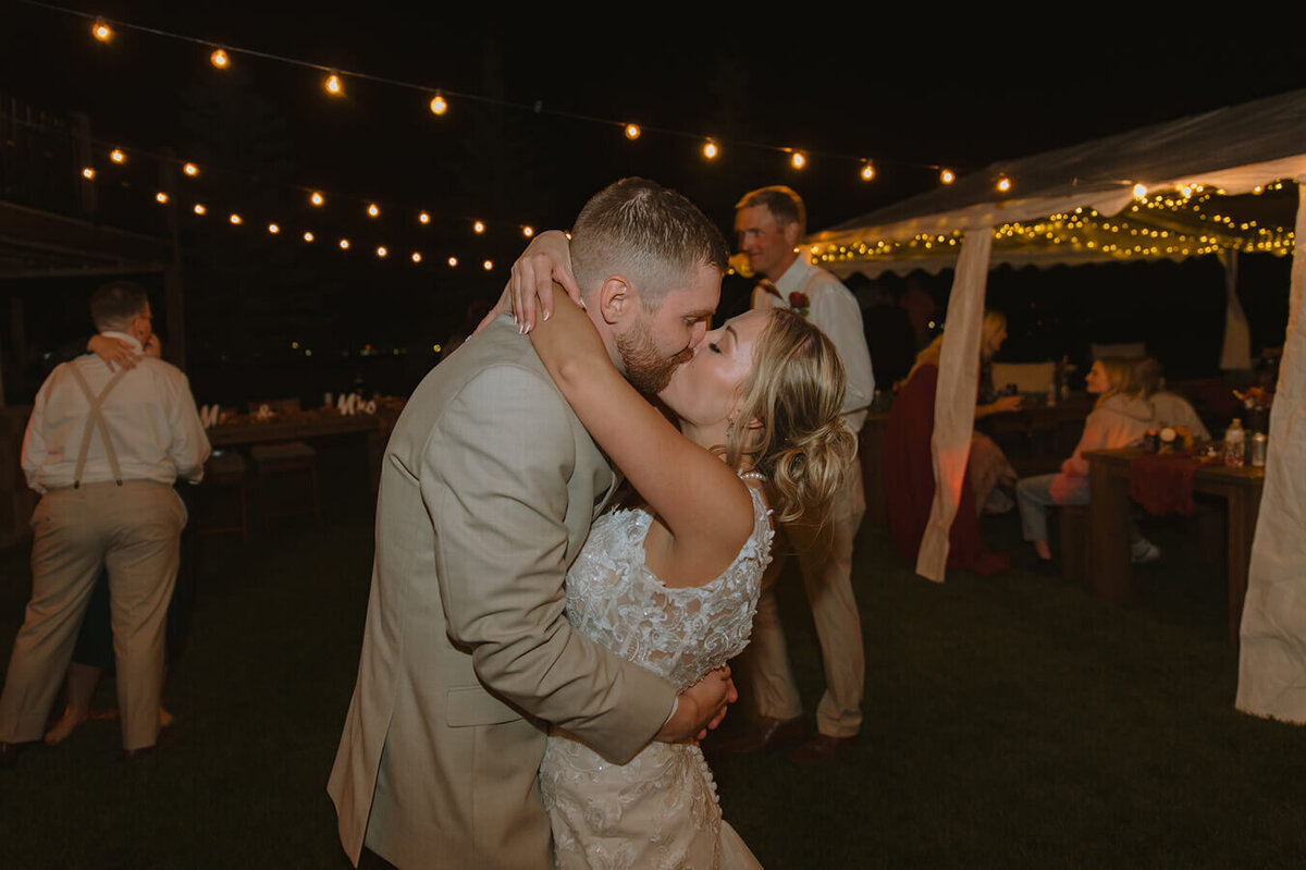 A flash photo of a bride and groom kissing at their wedding reception at night.