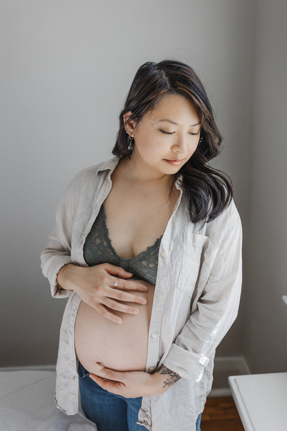Pregnant Asian woman wearing jeans and a green lace bralette  and beige shirt
