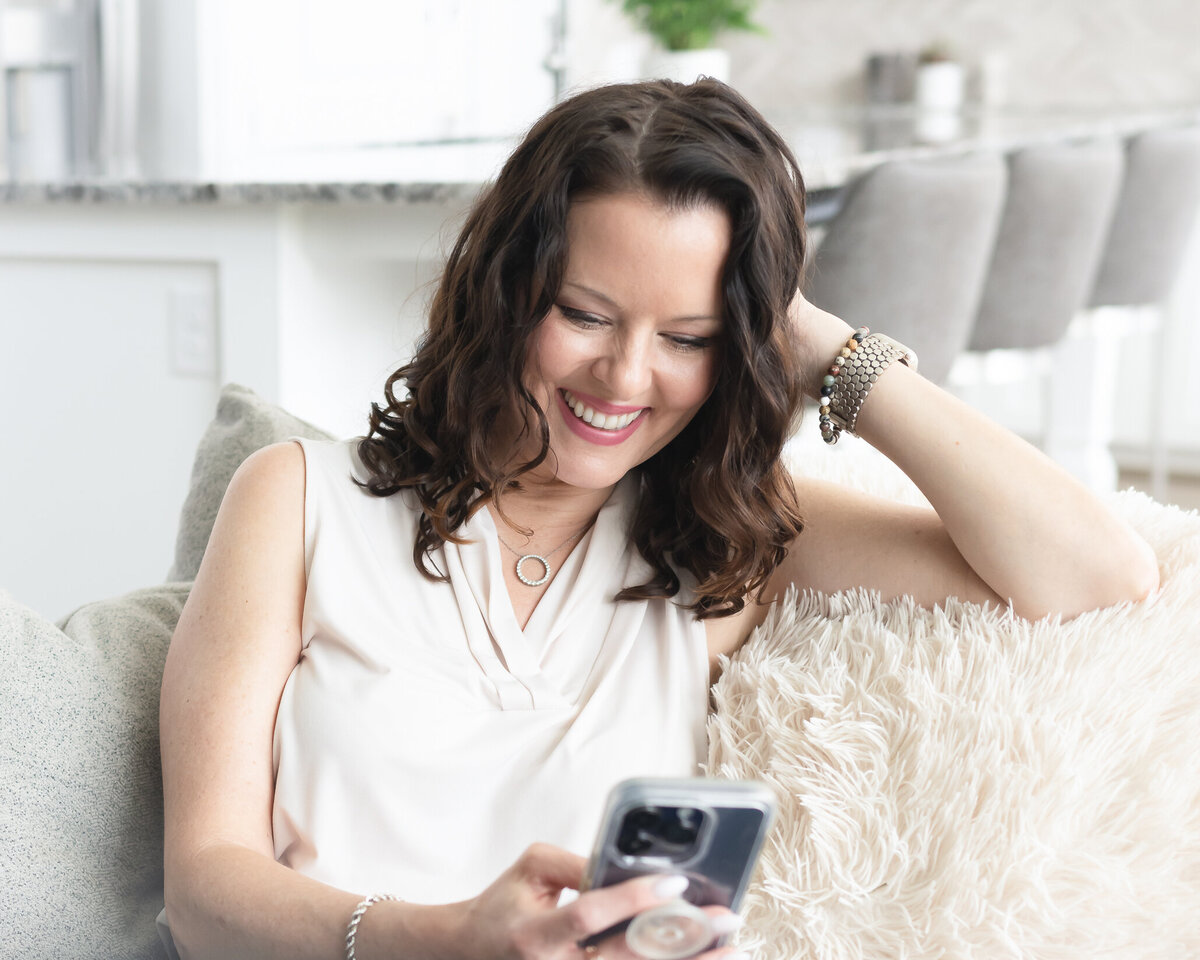 femaile business owner looking at her phone and smiling while sitting on the sofa