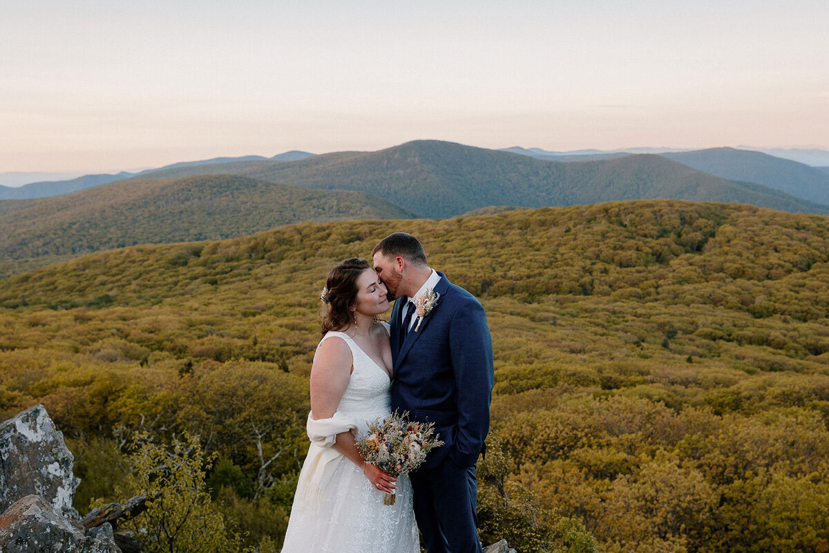 A bride and groom snuggling in front of the Blur Ridge Mountains in Shenandoah