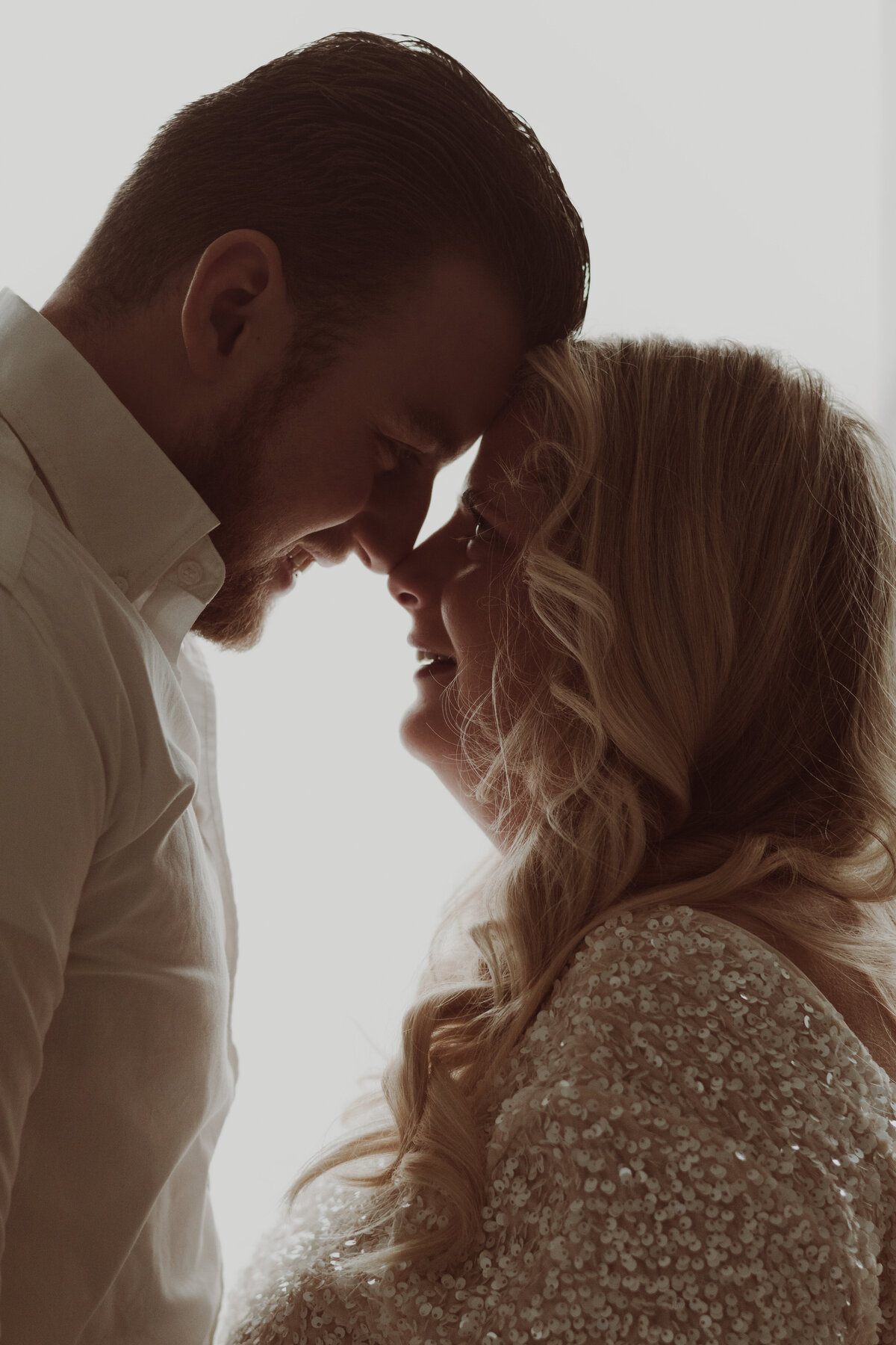 Een man en vrouw omarmen elkaar voor een witte achtergrond, stralend van liefde en verbondenheid.
