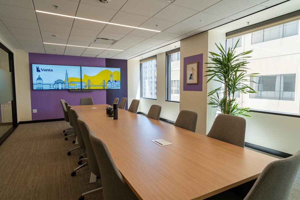 Large conference room with purple accent wall, cityscape display screens, and grey chairs around a long table.