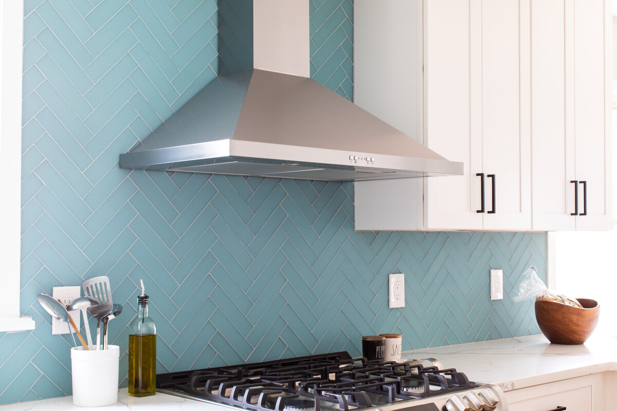 The kitchen is adorned with a full-height blue glass herringbone tile backsplash and Borghini Silver quartz countertops.