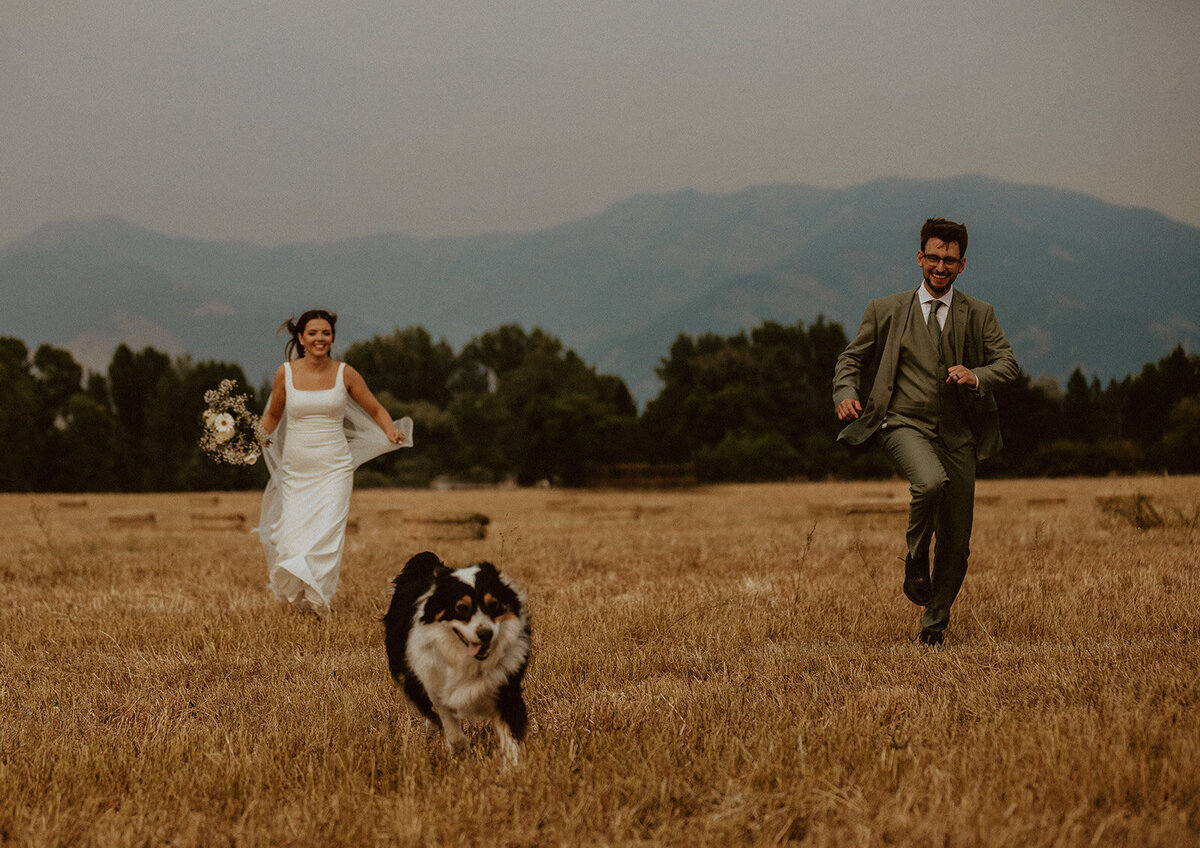 couple runs in field with dog in montana
