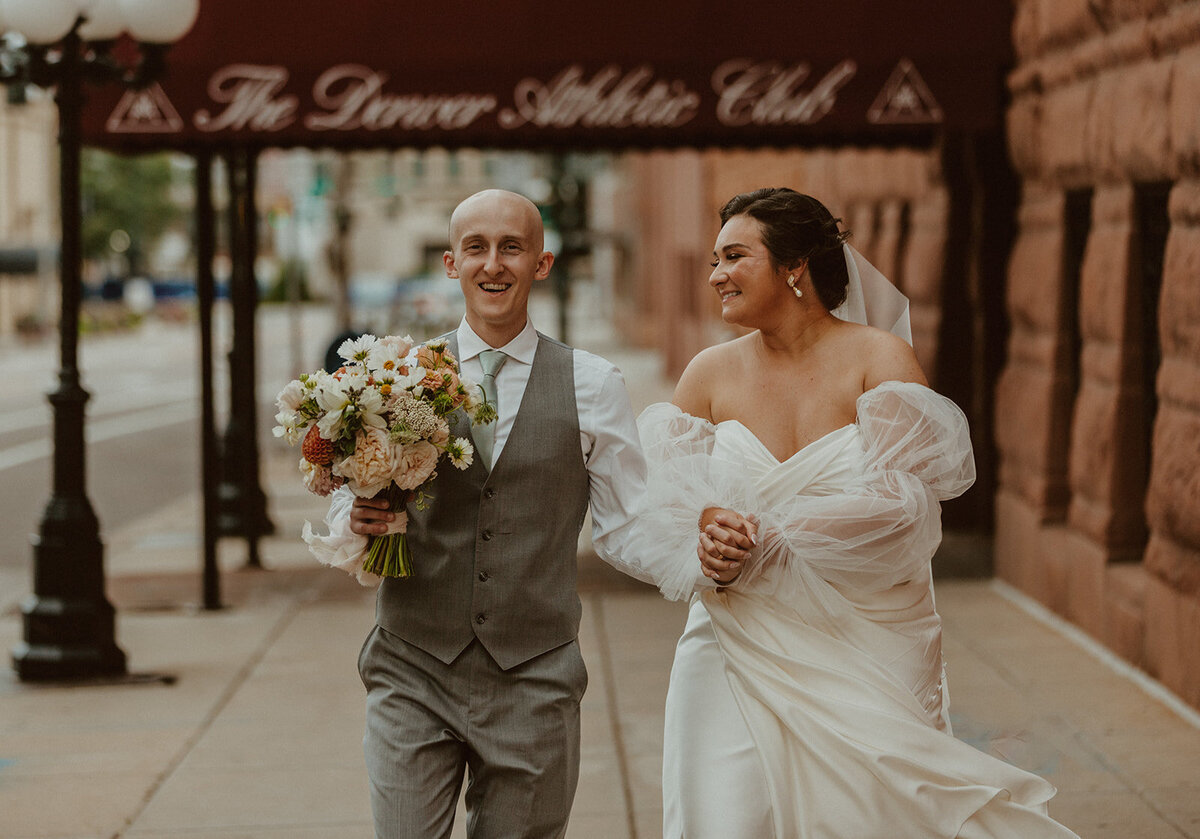 bride and groom walk down street outside of denver athletic club