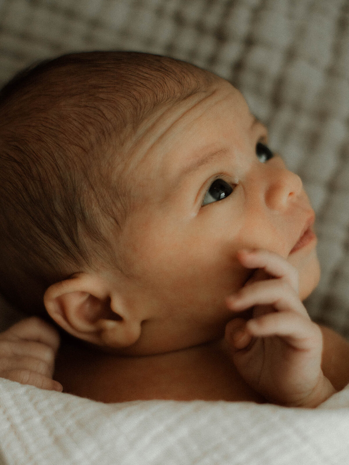 Portrait of a baby's face with his little hand resting on his cheek while he's looking up.