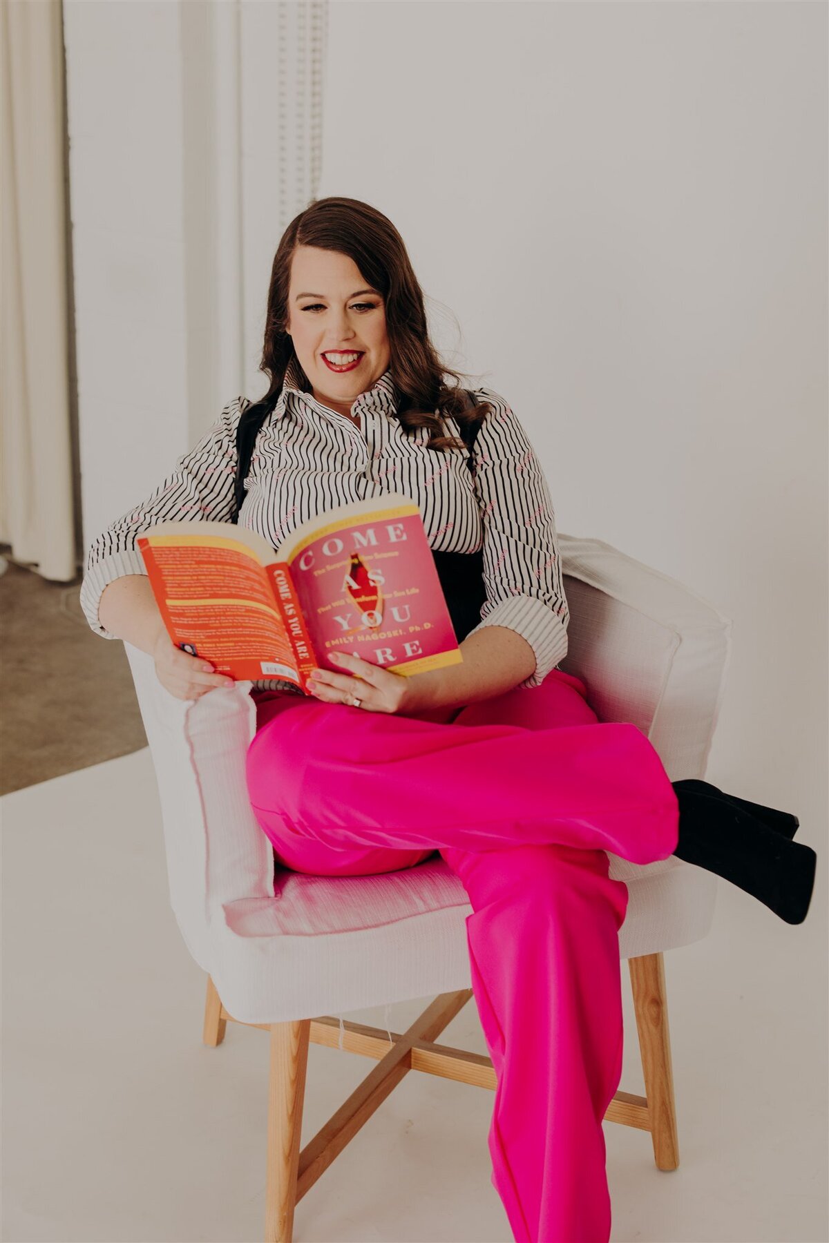 woman in striped shirting reading a book in a white chair