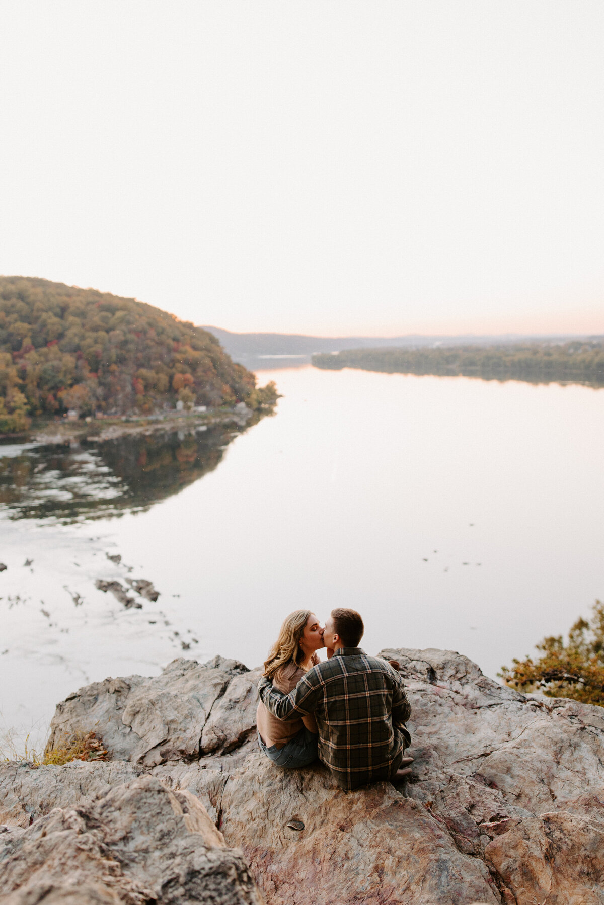 couple sitting on rocks overlooking the water as they kiss