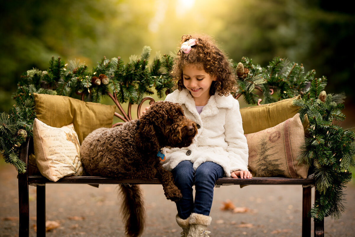Curly haired girl seated on a bench with her puppy during a Christmas photoshoot in Seattle WA.