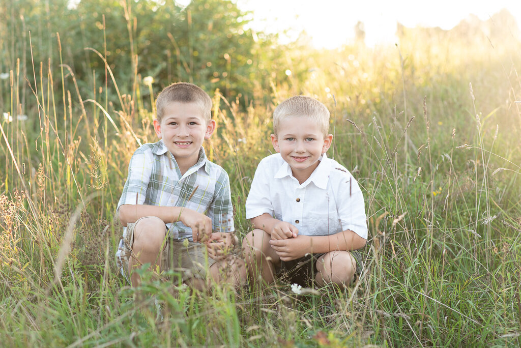Brothers squatting together in field at sunset