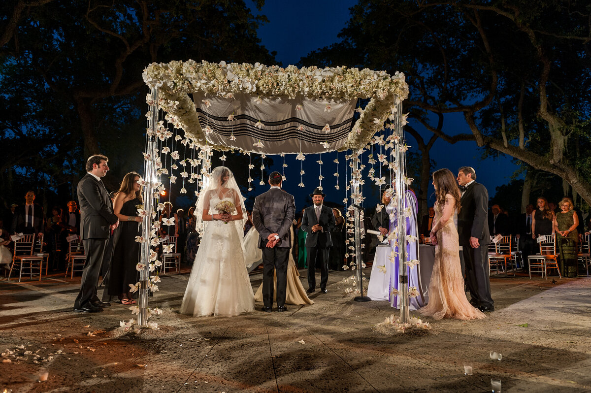 Jewish wedding ceremony under a floral chuppah with guests in attendance, photographed by Rodrigo Varela Photography.